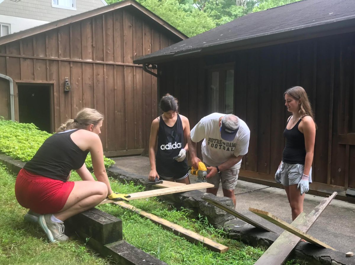 Ana Hudspeth, Emilia Reutebuch, and Sophia Uberta help cut a wooden board to replace a rotted handrail support on the Appalachia mission trip.
