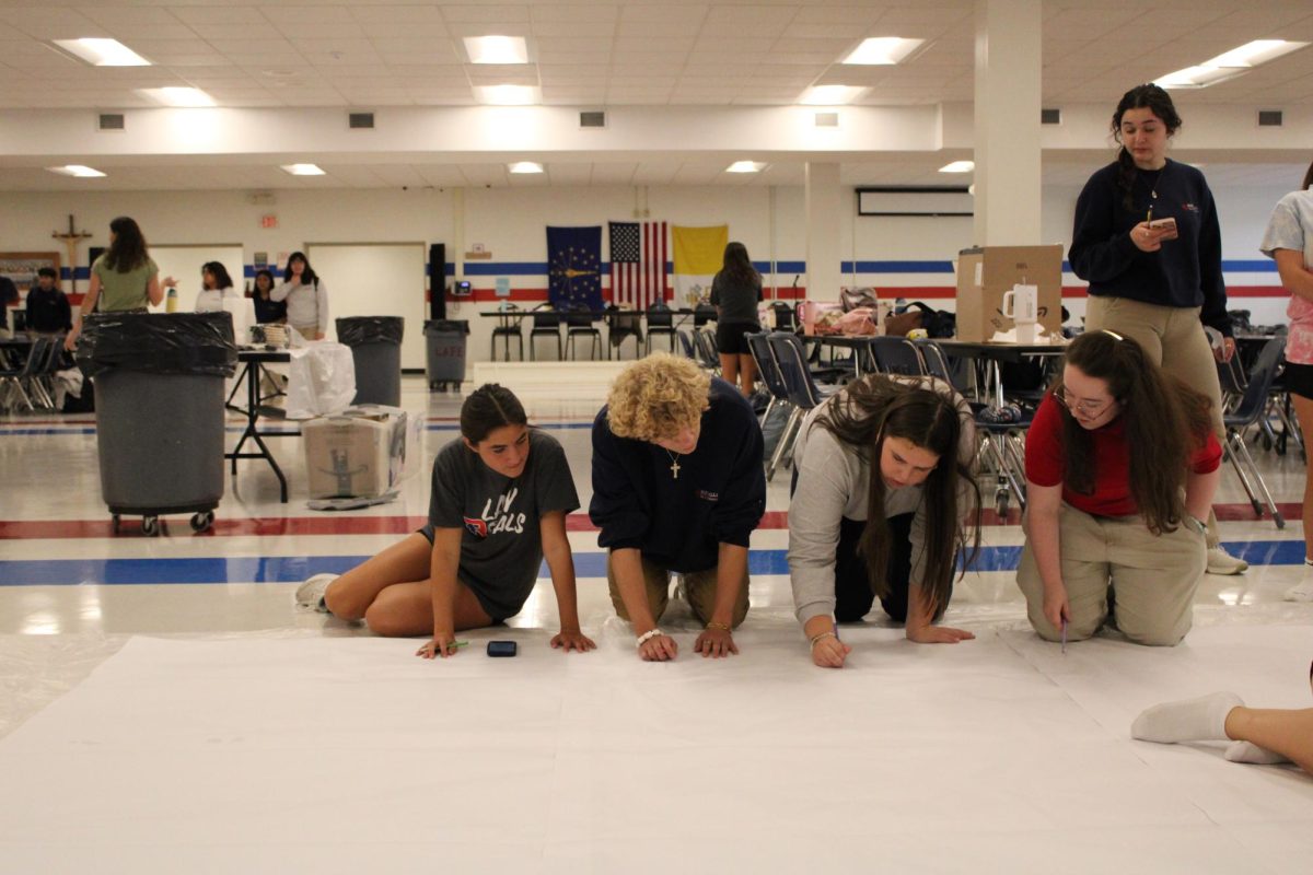 Juniors Cecelia Schoettle, Brennan Pierle, Lydia Traylor, and Jenna Stone work on painting a run-through banner for the Homecoming game.